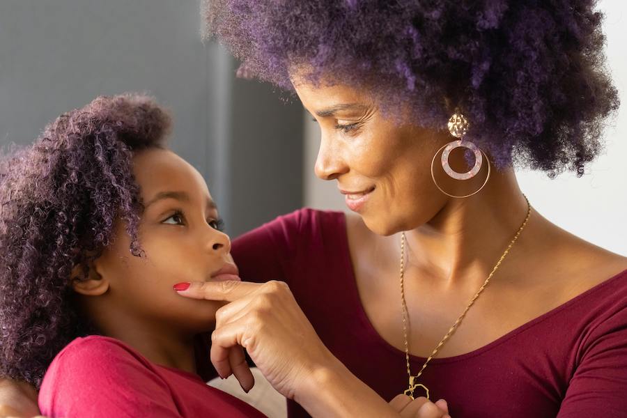 a mother looking into her daughter's eyes with a smile and her hand on her chin